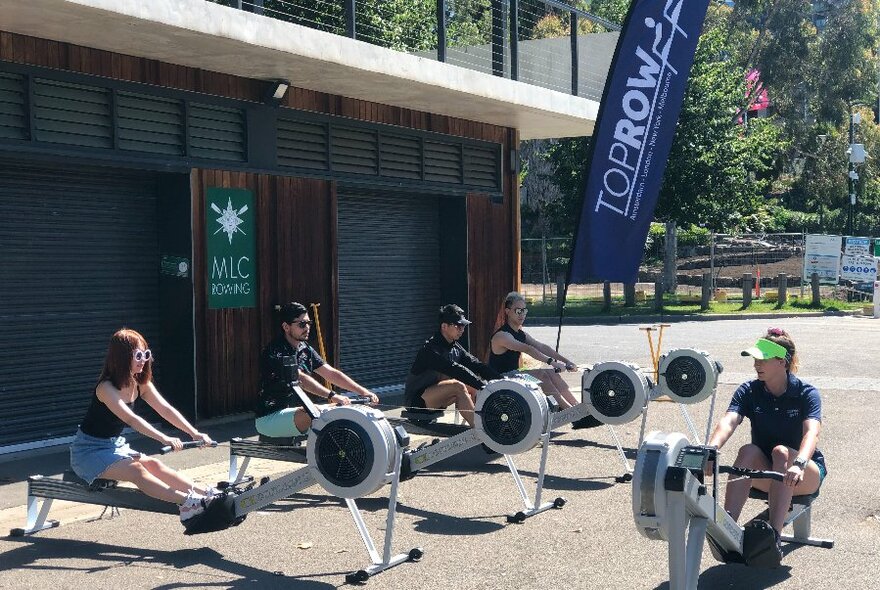 An instructor leading a class with four people on rowing machines. 