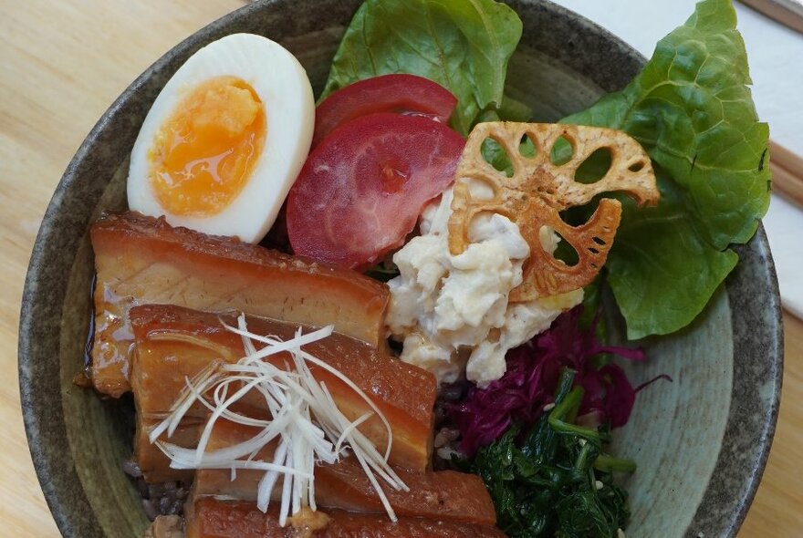 Overhead view of a curry bowl with sliced belly pork, a boiled egg, potato salad and lettuce.