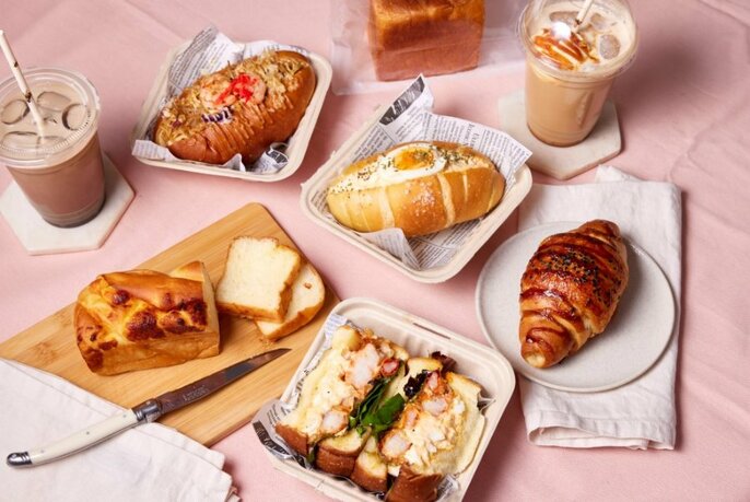 Baked savoury and sweet goods and pastries on a pink tablecloth with iced drinks in plastic cups on coasters.