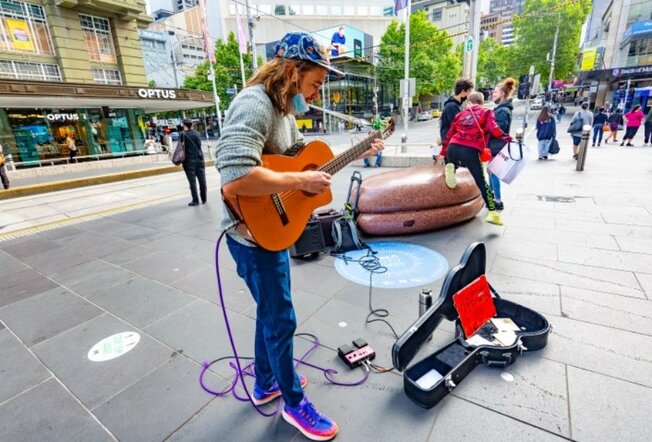 A busker on Bourke Street with a guitar and families in the background.