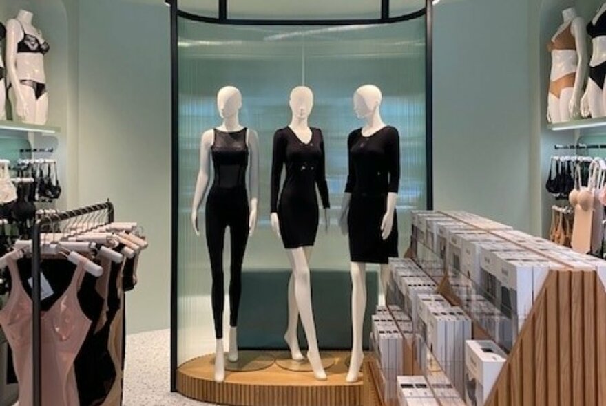Store interior with mannequins dressed in black, shelves of packaged items and displays of lingerie.