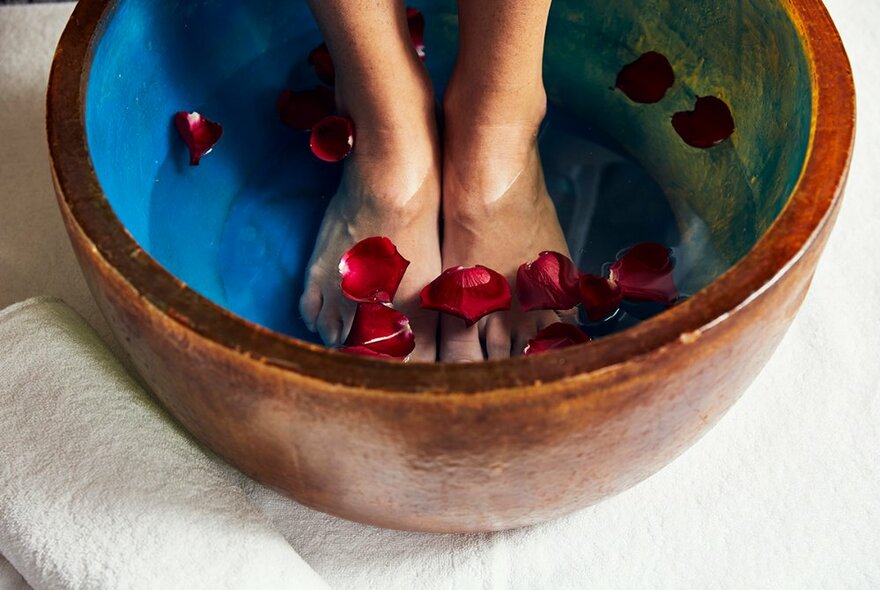 Feet resting in a round blue bowl of water with rose petals.
