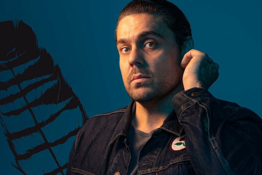 Singer and songwriter Dan Sultan looking blankly with his left hand to his ear. 