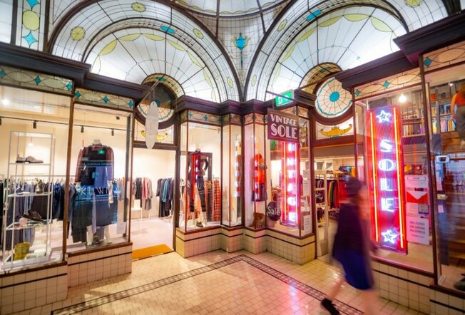 A blurred shopping walking past shops with stained glass arched windows and neon lights.