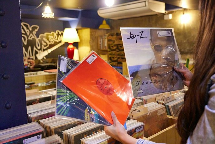 Someone holding up three records in a shop.