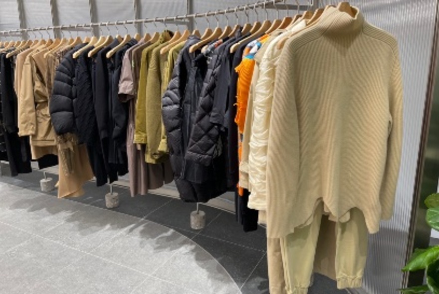 Long, curved rack of clothing in taupes, orange and black.