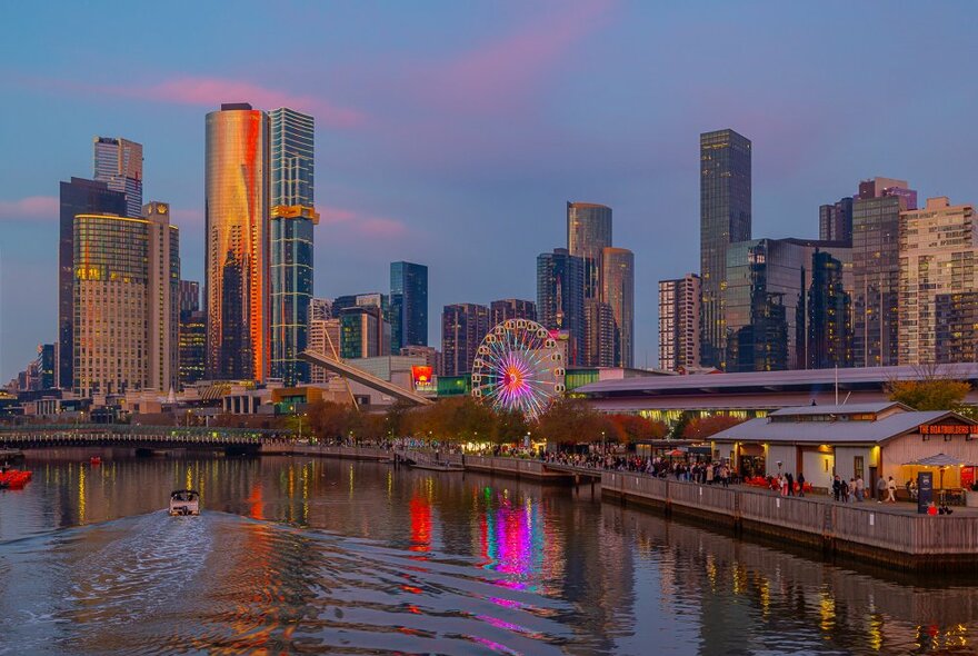 A view of a river at sunset with a Ferris wheel and a city skyline in the background