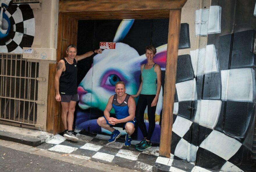 Three people in active wear posing outside laneway street art.