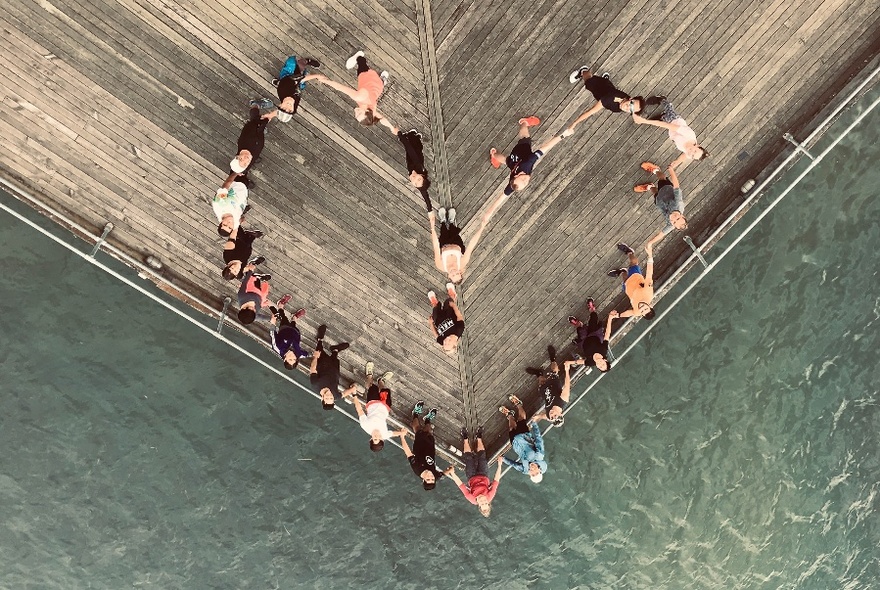 Looking down on a group of people who have formed a heart shape on the corner of a pier.