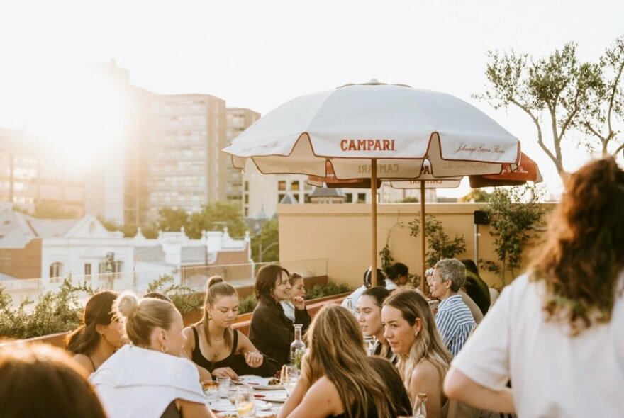Diners seated at tables at an outdoor rooftop bar in the fading evening sunlight.
