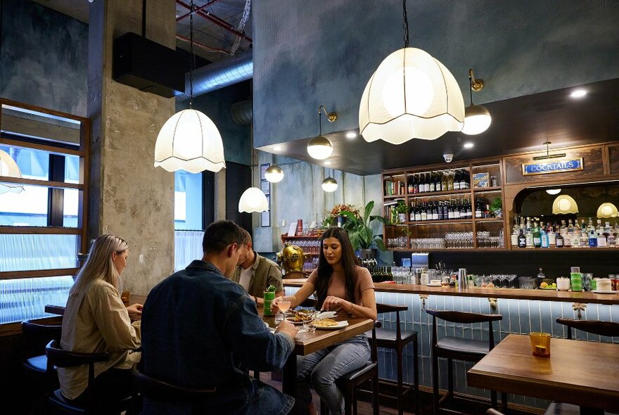 People dining in a restaurant with pendant lights and a blue tiled bar.