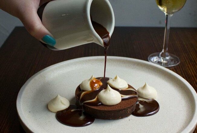 A chocolate dessert on a plate with a jug pouring over chocolate sauce.