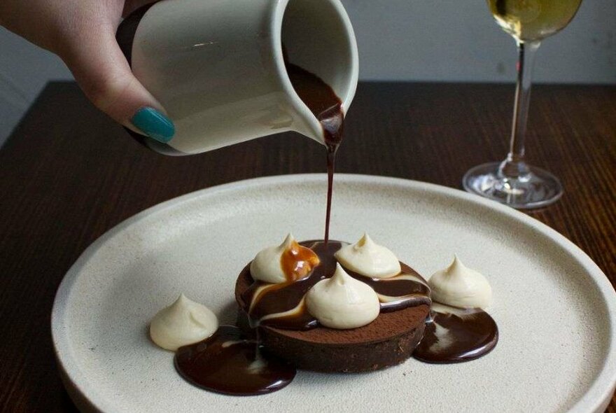 A chocolate dessert on a plate with a jug pouring over chocolate sauce.