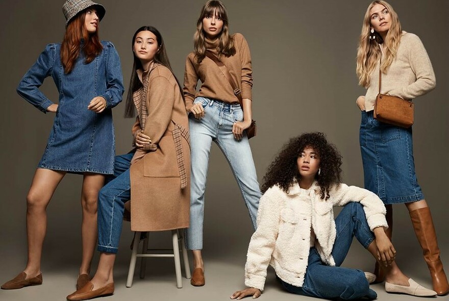 Group of young female models wearing denim and brown-themed jeans, jackets and dresses.