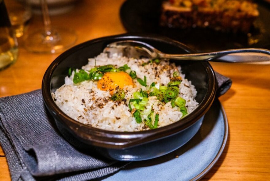 Black bowl of fried rice with spring onion and fried egg.