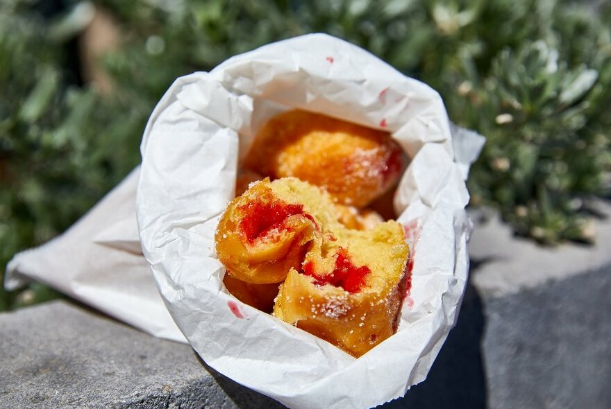 A white paper bag filled with hot jam donuts.