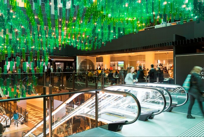 Green sculptural lightscape and escalators inside St. Collins Lane shopping centre.