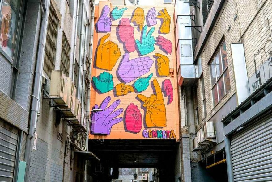 A street art mural with painted hand shapes in a laneway