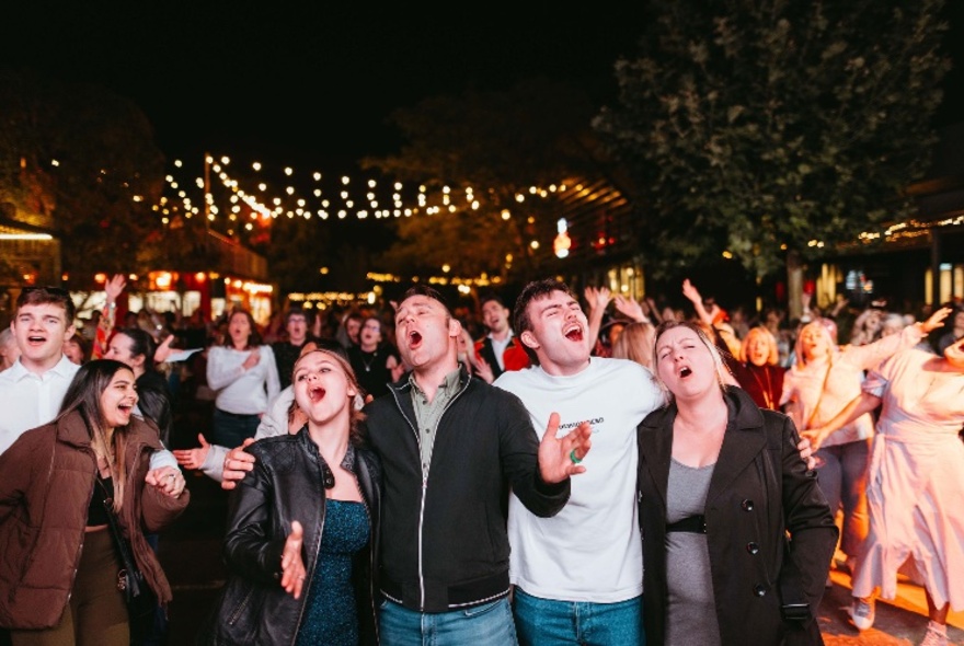 A crowd of people singing together in an open air outdoor space.