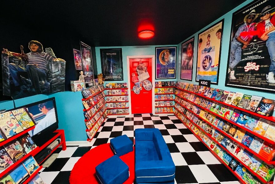 A replica interior of a video store with bright colours, a blue sofa and vintage movie posters. 