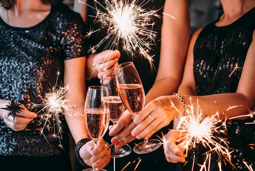Hands clinking glasses of pink bubbles, holding sparklers.