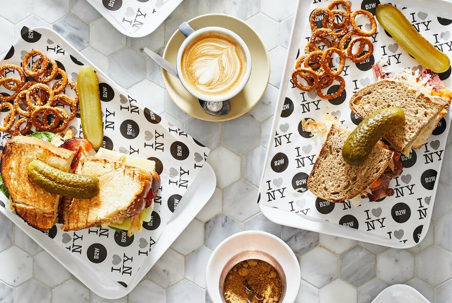 A cafe table set with coffee and sandwiches served with pretzels and pickles.
