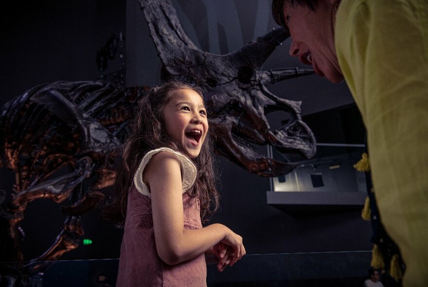 Child looking over right shoulder with delighted smile, dark dinosaur model behind.