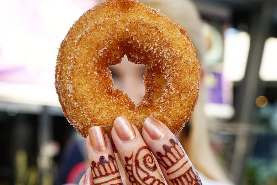 A donut being held up by three fingers that have been decorated with henna tattoos.