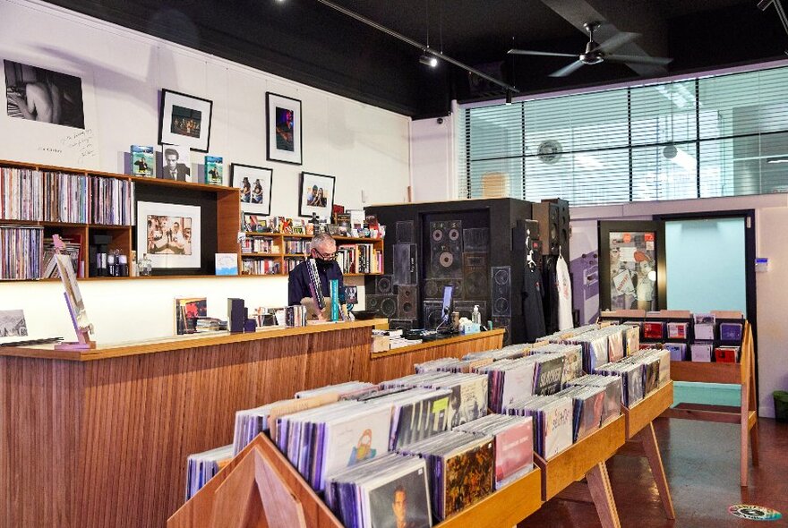 A man standing behind a counter in a shop surrounded by shelves of vinyl records