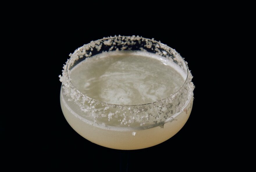 A margarita cocktail in a glass, rimmed with salt flakes.