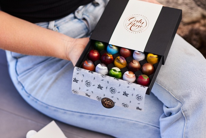 Hands holding an open box of multicoloured chocolates.