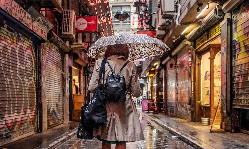 A woman walking through a laneway with a leopard print umbrella.