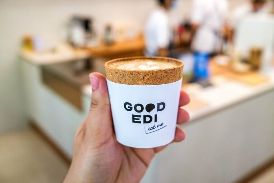 A person's hand holding an edible coffee cup that looks like cork.