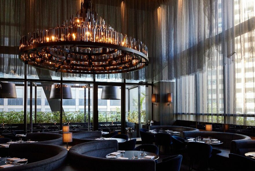 An elegant restaurant with black booths and a giant chandelier. 