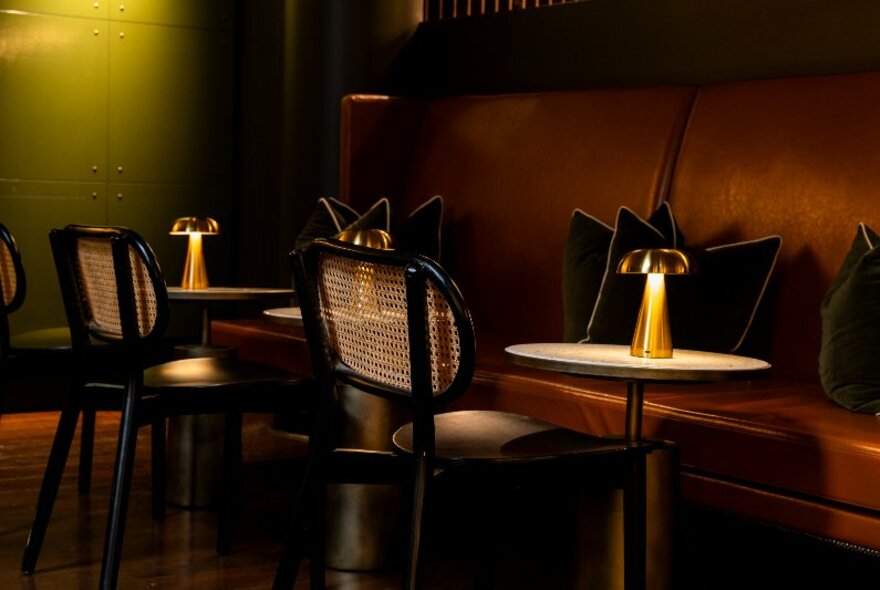 Soft and moody lighting in a restaurant interior, with individual chairs placed under small round tables facing comfortable banquette seating.
