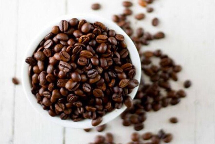 Overhead view of coffee beans spilling over a full cup of beans.