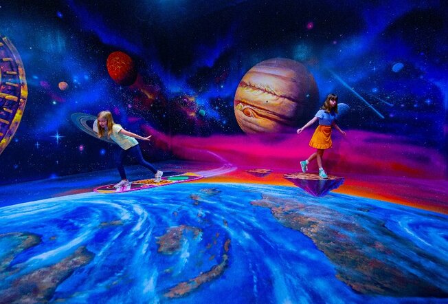 Two children standing in front of a mural painted as outer space