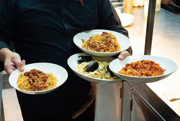 Waiter carrying four bowls of pasta.