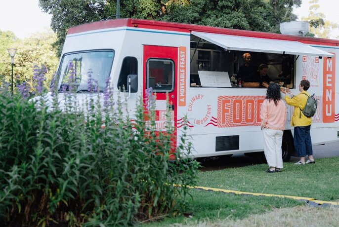 Two people waiting at a food truck in a garden setting. 