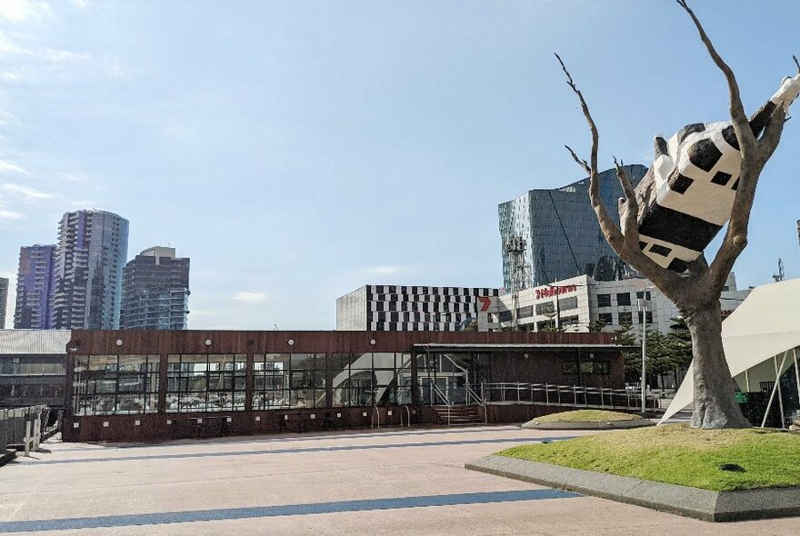 Exterior of the ferry terminal at Docklands, with the Cow up a Tree sculpture in the foreground.
