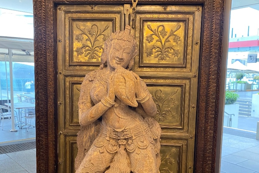 A large clay buddha statue in front of an embossed gold and wooden panel. 