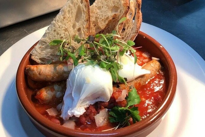 A plate of food in a terracotta bowl with a poached egg on top and sourdough bread on the side.