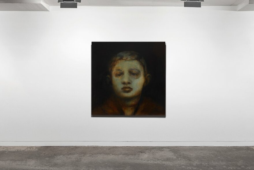 Painting of a child's face, hanging on a gallery's white wall.