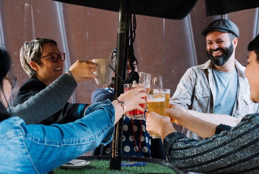 Four people cheering drinks at a table under an umbrella. 