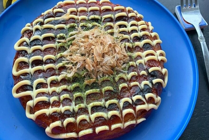 Japanese savoury pancake (okonomiyaki) garnished with mayonnaise, on a plate.