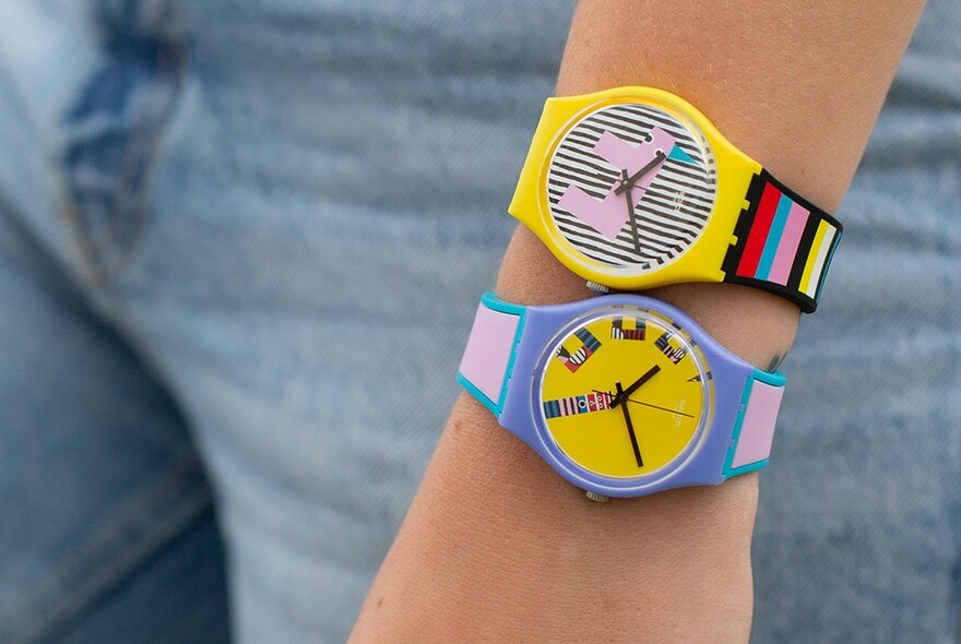 Model's wrist with two brightly coloured geometric Swatches with no digits.