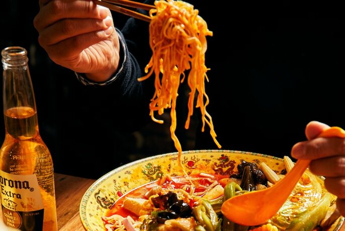 Person using chopsticks to eat noodles from a plate of Chinese food. 