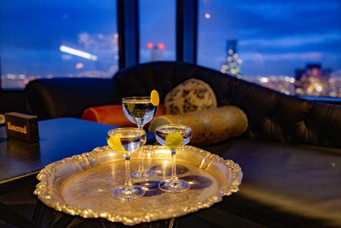 Three drinks on a silver tray at a 55th floor cocktail bar.