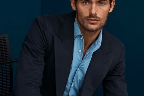Man in dark blue suit jacket with light blue, unbuttoned shirt; image cropped just above his eyes.