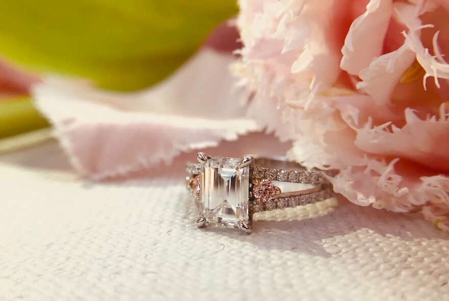 A square-cut diamond ring resting next to a silk flower.